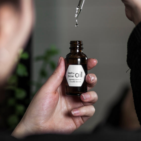 hand holding a bottle labeled 'lash + brow oil' with a dropper applicator
